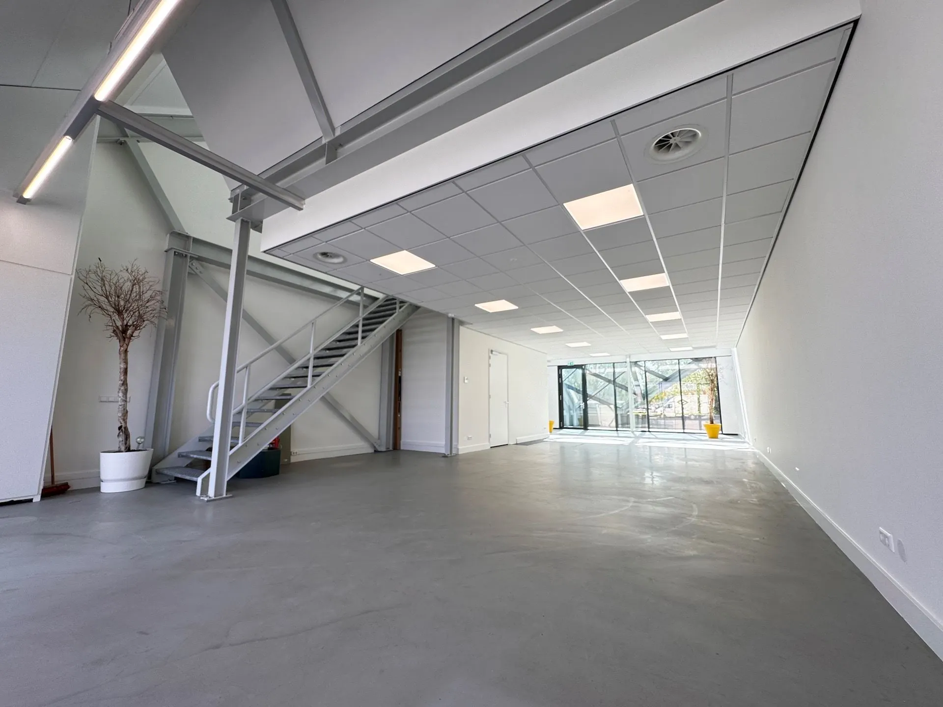 Lichte, lege kantoorruimte in het Mart Stamhof-gebouw met een metalen trap en grote glazen gevel.